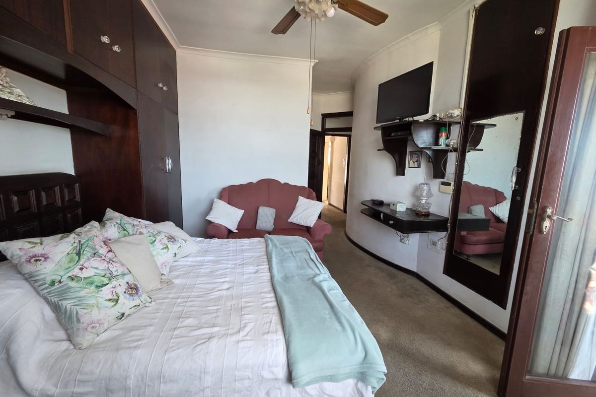 A bedroom featuring built-in dark wood cabinetry, a ceiling fan, and wall-mounted shelving, with direct access to an adjoining space.