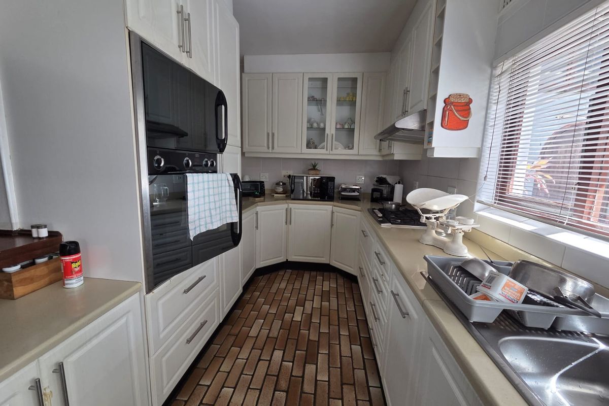 A functional kitchen featuring white cabinetry, built-in oven, gas hob, extractor fan, and a stainless steel sink with brick-style flooring.