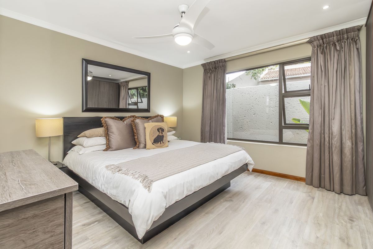 A well-maintained bedroom featuring laminate flooring, built-in cupboards, a ceiling fan, and large windows allowing natural light.