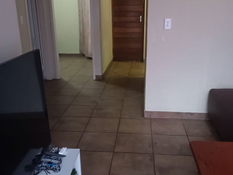 A functional hallway featuring tiled flooring and a wooden door, providing access to adjacent rooms within the apartment.