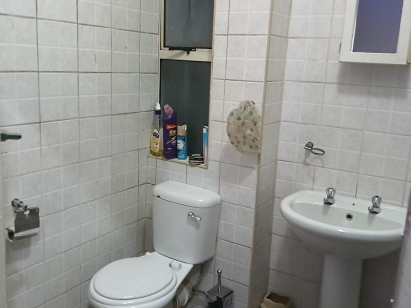 A compact bathroom featuring a pedestal basin, toilet, and full-height wall tiling. The space would benefit from modern updates to finishes and fixtures.