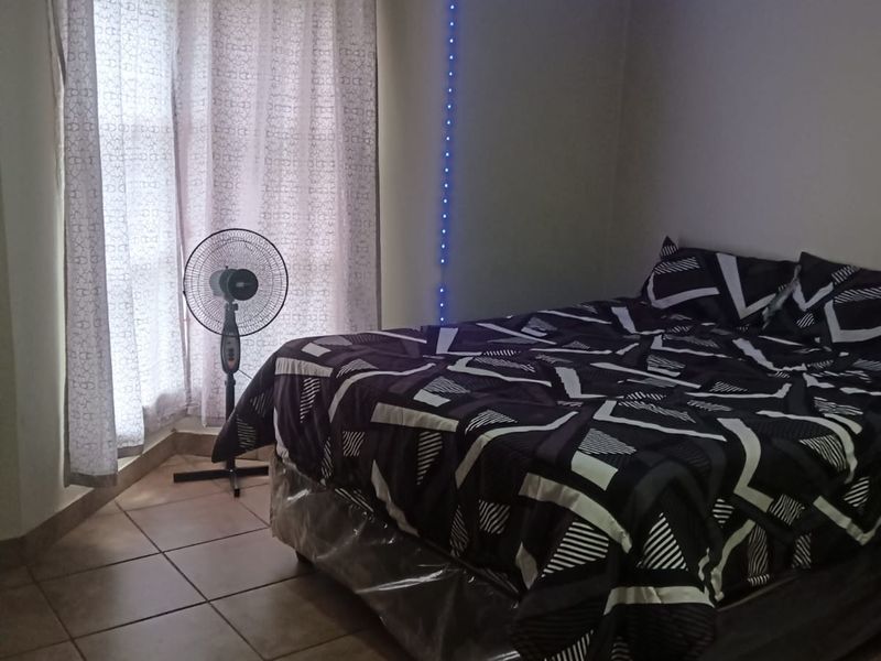 A bedroom featuring tiled flooring and window curtain rails, illuminated by ambient LED strip lighting.