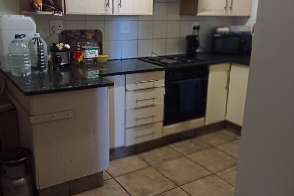 A functional kitchen featuring light-toned cabinetry, granite countertops, tiled flooring, and a built-in oven with a gas hob and extractor fan.