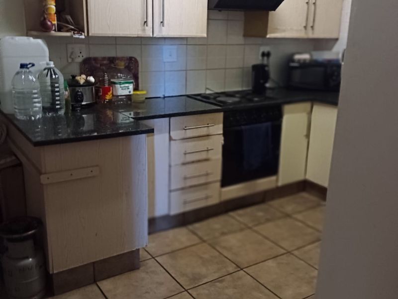 A functional kitchen featuring light-toned cabinetry, granite countertops, tiled flooring, and a built-in oven with a gas hob and extractor fan.