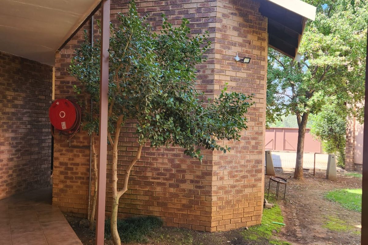 A view of the rear exterior brick facade featuring a covered tiled patio area, a fire hose reel, and surrounding garden space.