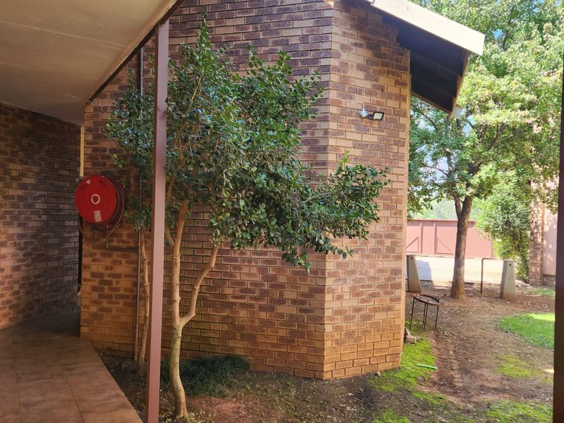 A view of the rear exterior brick facade featuring a covered tiled patio area, a fire hose reel, and surrounding garden space.