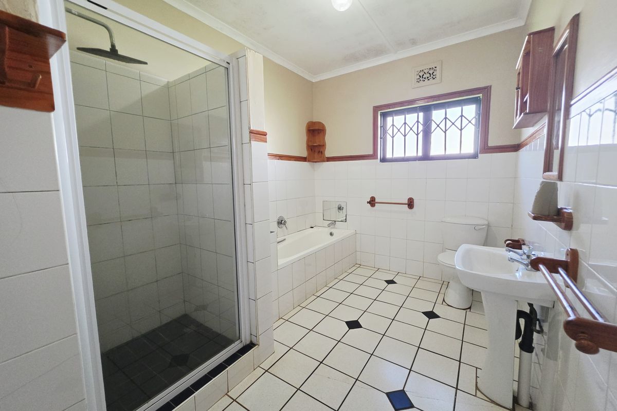 A functional bathroom featuring a separate shower enclosure, built-in bathtub, pedestal sink, and classic tiled flooring with decorative accents.