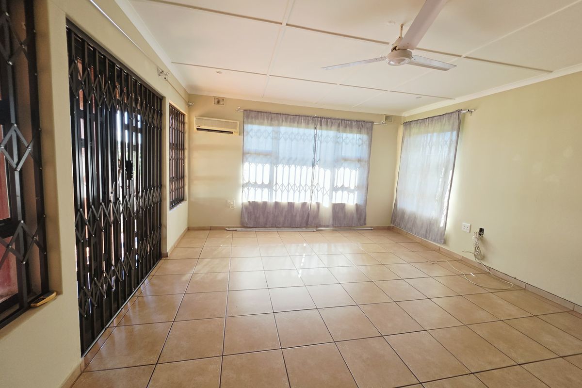 Spacious, empty living area featuring tiled flooring, a ceiling fan, split-system air conditioning, and secure window and door treatments.