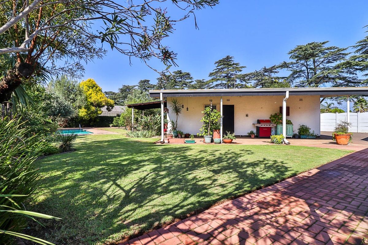 A spacious rear garden featuring a covered patio area, paved walkway, and a swimming pool, offering a private outdoor entertainment space.