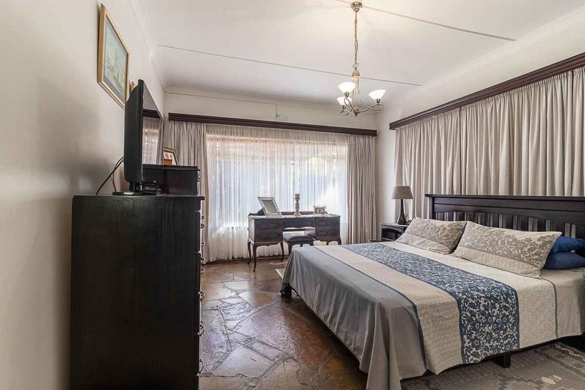 A spacious bedroom featuring unique flagstone flooring, large windows with curtain tracks, and a central ceiling light fixture.