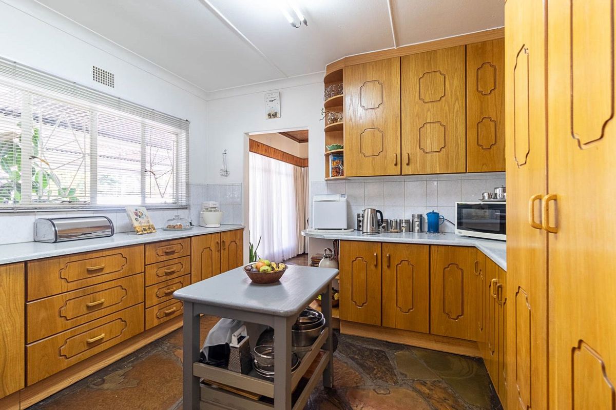 A functional kitchen featuring traditional timber cabinetry, tiled splashbacks, and a unique natural stone floor, offering a classic aesthetic with ample storage space.