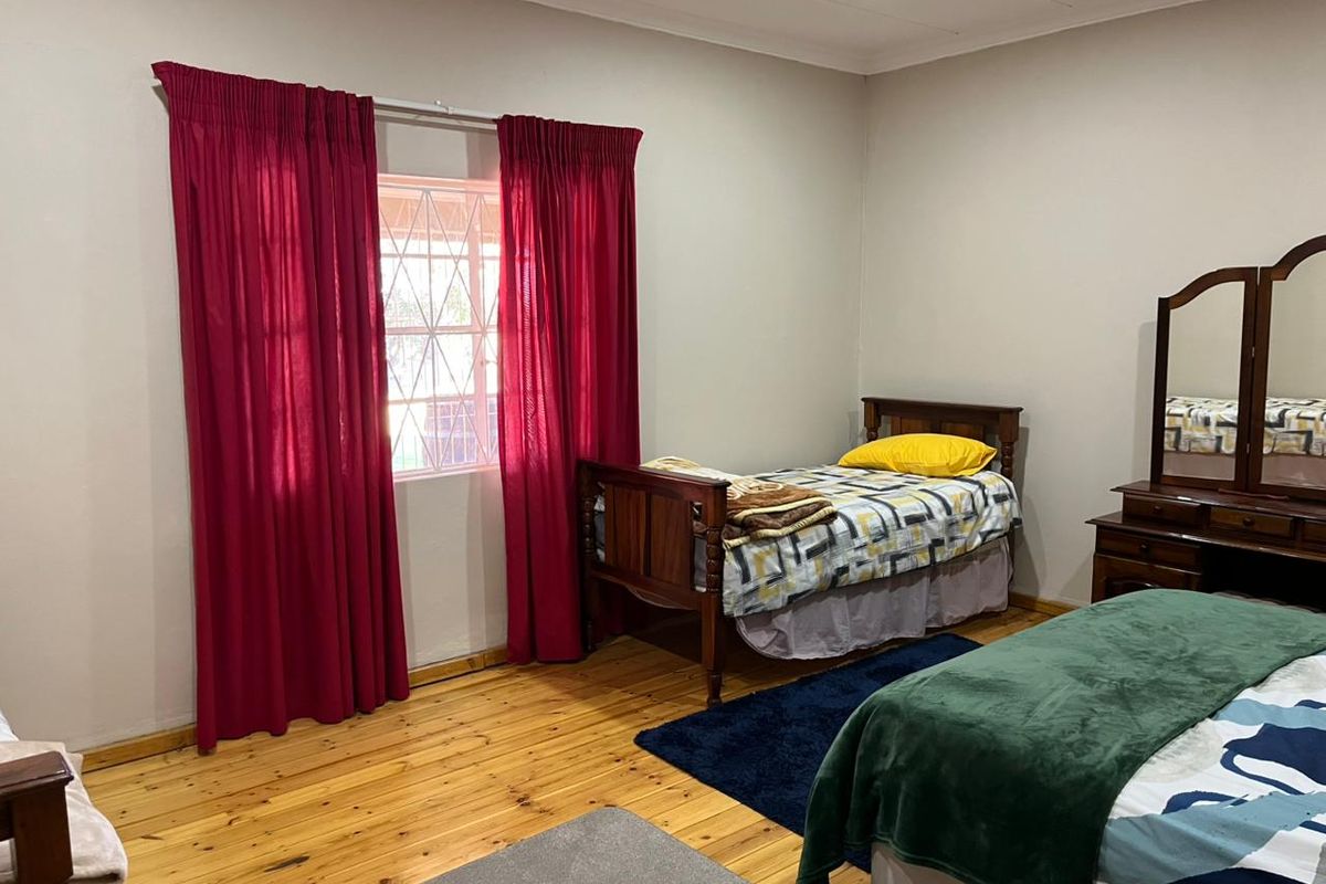 A bedroom featuring polished wooden flooring, neutral wall tones, and a window fitted with security bars.