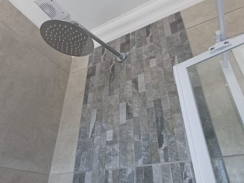 A modern shower enclosure featuring a rain shower head, a decorative mosaic tile accent wall, and large format neutral wall tiles.