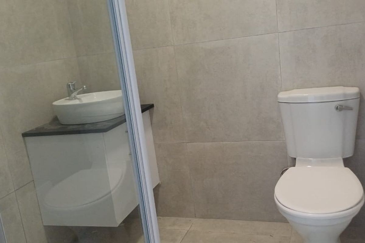 A clean, modern bathroom featuring neutral wall and floor tiles, a white toilet, and a vanity with a basin.
