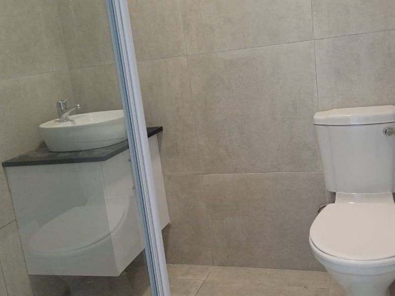 A clean, modern bathroom featuring neutral wall and floor tiles, a white toilet, and a vanity with a basin.