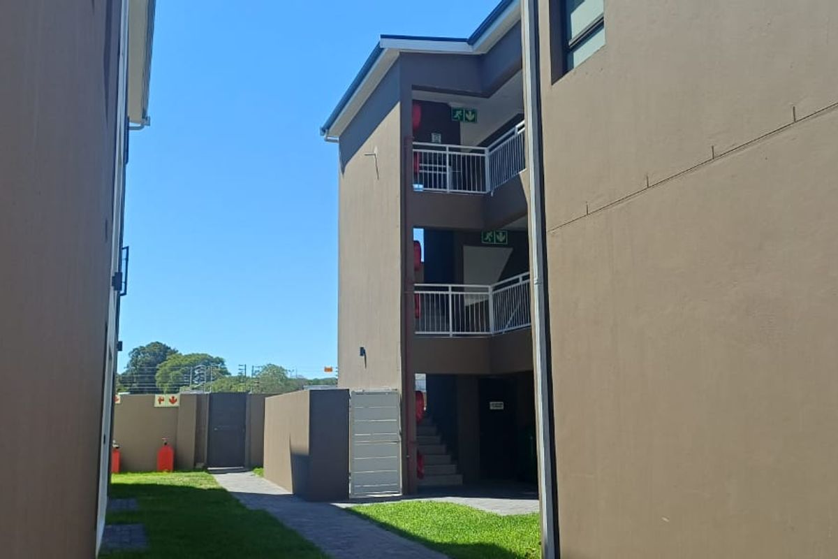 Exterior view of an apartment building featuring a multi-level staircase, balcony railings, and a paved walkway through a landscaped area.