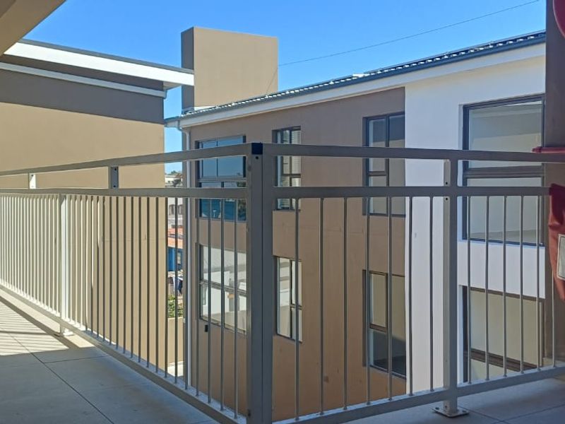 A clean, modern apartment balcony featuring a white metal balustrade, tiled flooring, and essential fire safety equipment.