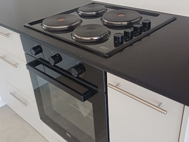 A modern kitchen featuring a built-in electric oven, hob, sleek stone countertops, and light-toned cabinetry with stainless steel hardware.