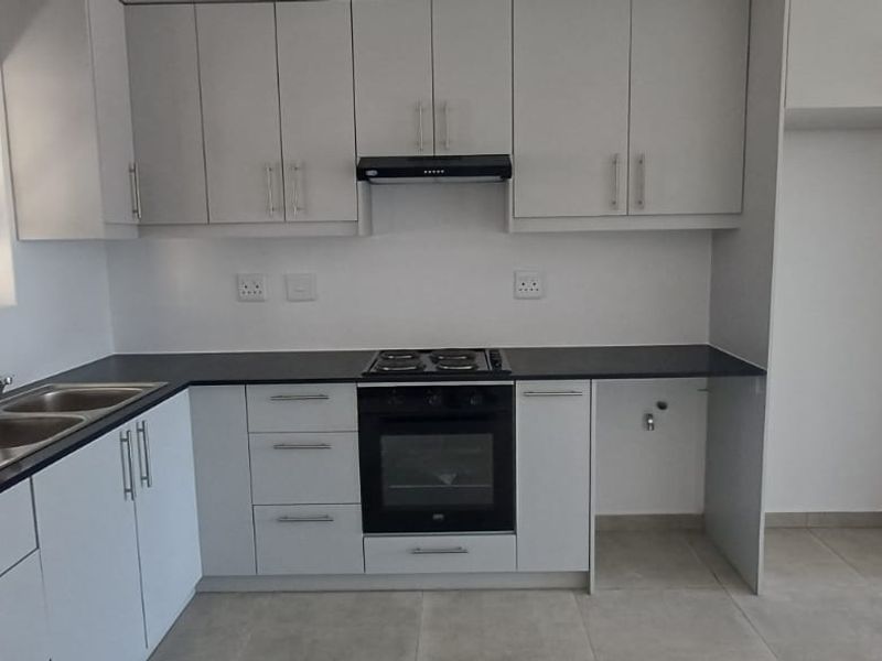 Modern kitchen featuring white cabinetry, dark laminate countertops, integrated oven and hob, extractor fan, and double sink with tiled flooring.