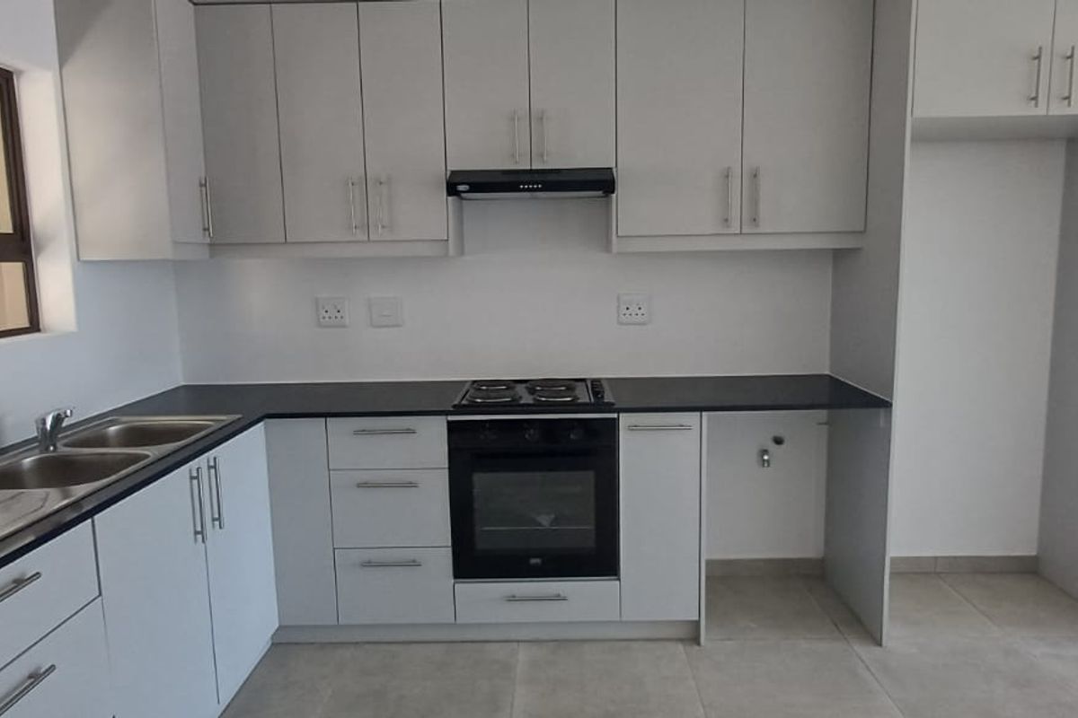 Modern kitchen featuring white cabinetry, dark laminate countertops, integrated oven and hob, extractor fan, and double sink with tiled flooring.