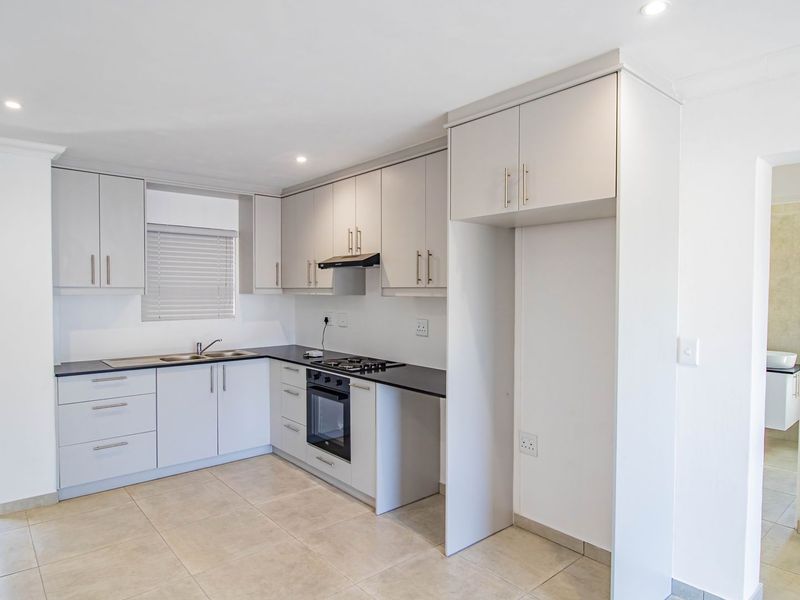 Modern kitchen featuring light grey cabinetry, dark countertops, built-in oven with gas hob, and tiled flooring, with direct access to a balcony.