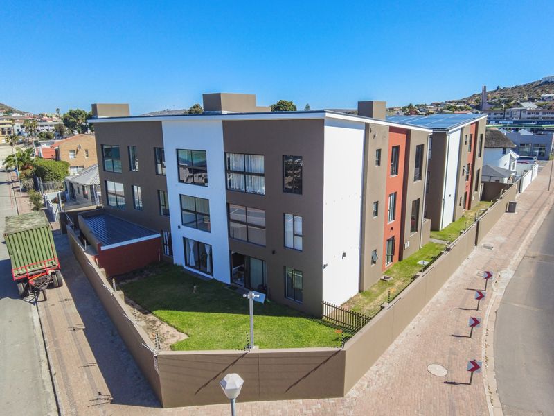 Aerial view of a modern multi-story apartment complex featuring a secure perimeter wall, electric fencing, and solar panel installation on the roof.