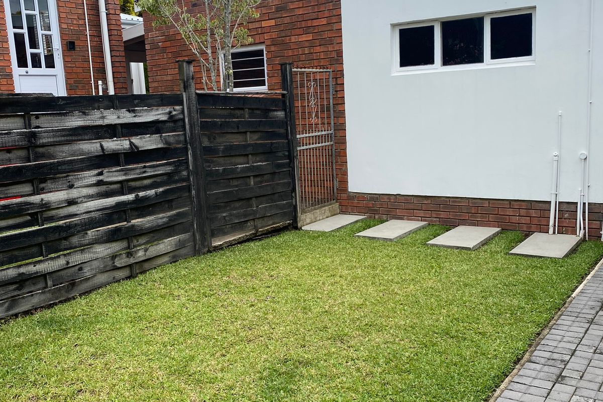 A private rear garden area featuring a well-maintained lawn, paved pathway, and a combination of brick and rendered exterior walls.