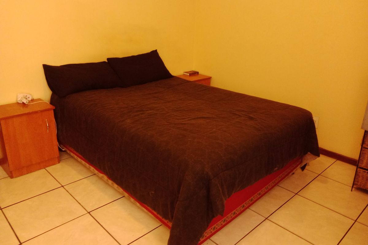 A simple bedroom featuring tiled flooring and yellow wall paint, providing a functional space for rest.