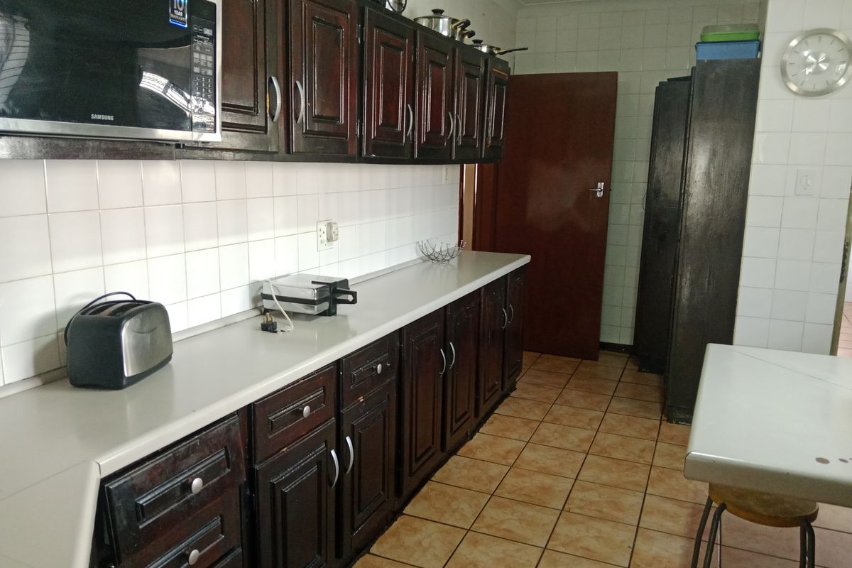 A functional kitchen featuring dark wood cabinetry, tiled splashbacks, and tiled flooring, providing ample storage and workspace for daily meal preparation.