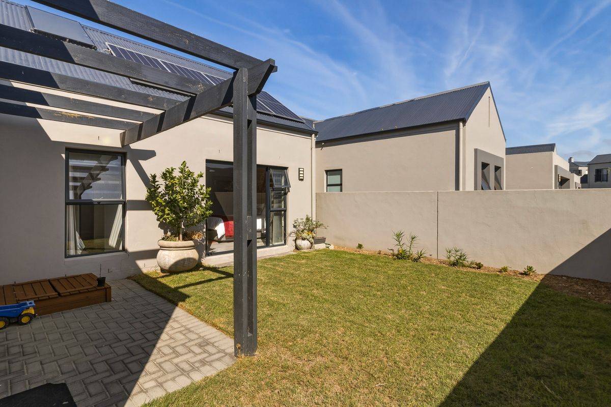 A well-maintained rear garden featuring a paved patio area, a timber pergola, and a private boundary wall with solar panels on the roof.