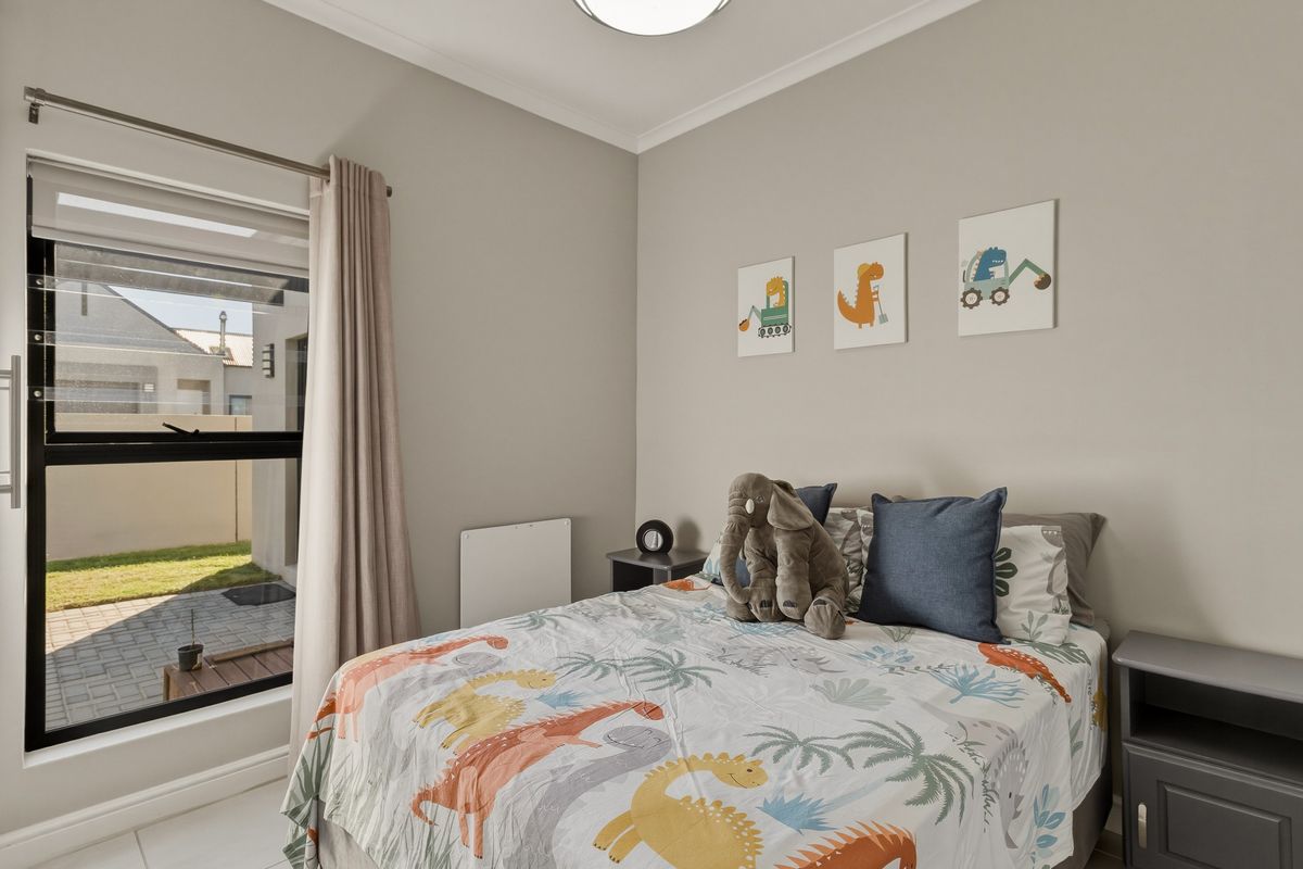 A well-maintained bedroom featuring neutral wall tones, tiled flooring, and a large aluminium-framed window providing natural light and garden views.