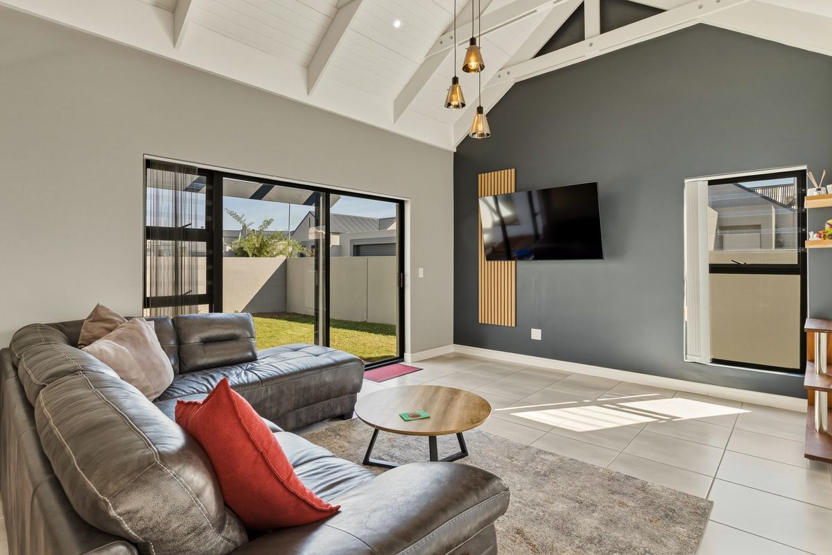 Modern living room featuring a high vaulted ceiling with exposed trusses, large sliding glass doors leading to the garden, and a stylish feature wall.