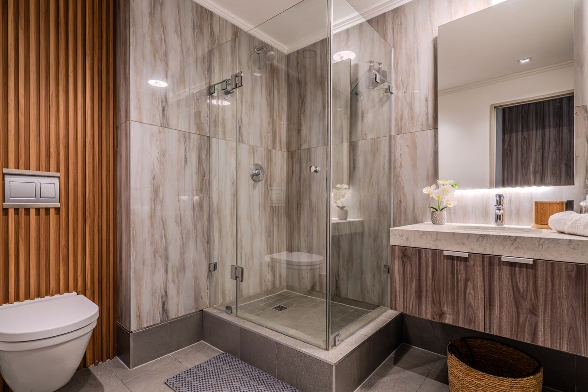 Modern bathroom featuring a glass-enclosed walk-in shower, wall-mounted toilet, floating vanity with stone countertop, and decorative timber slat wall paneling.