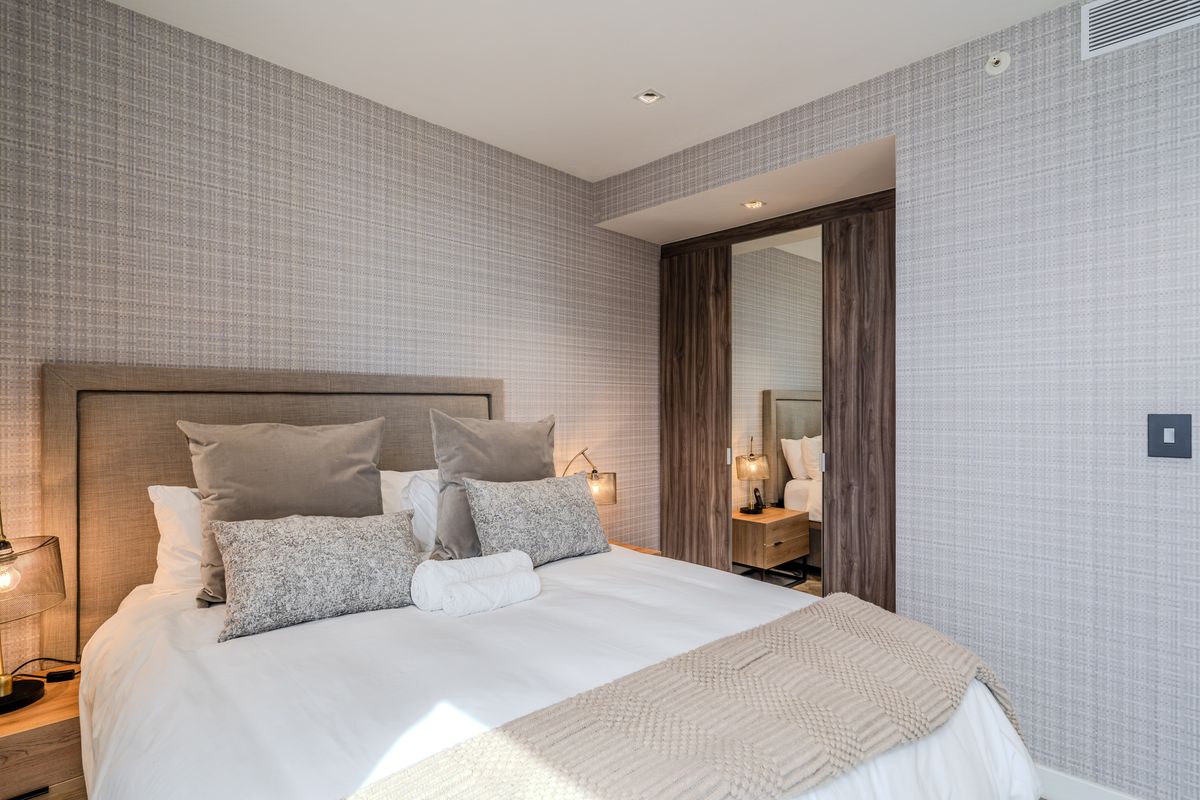 A well-appointed bedroom featuring textured wallpaper, recessed ceiling lighting, and built-in wooden wardrobe cabinetry with mirrored panels.