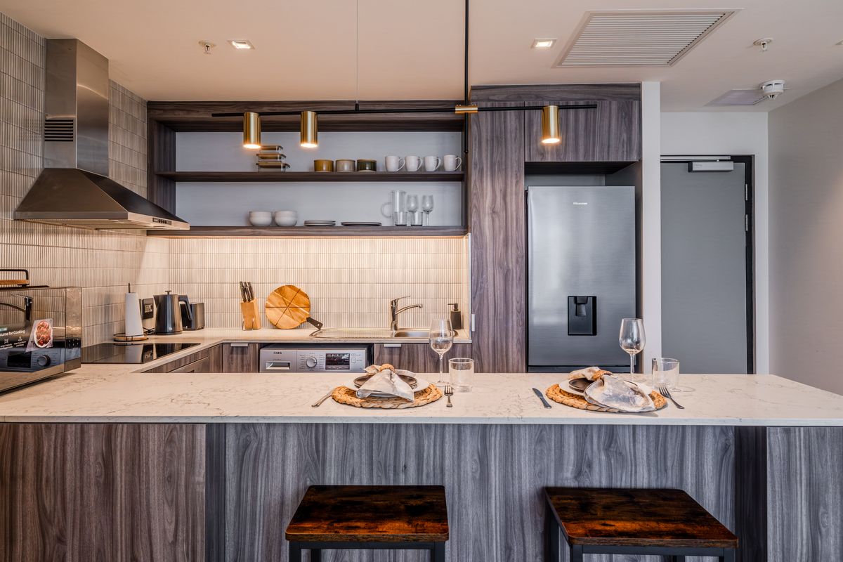 Modern kitchen featuring wood-grain cabinetry, stone countertops, integrated appliances, and a breakfast bar with pendant lighting.