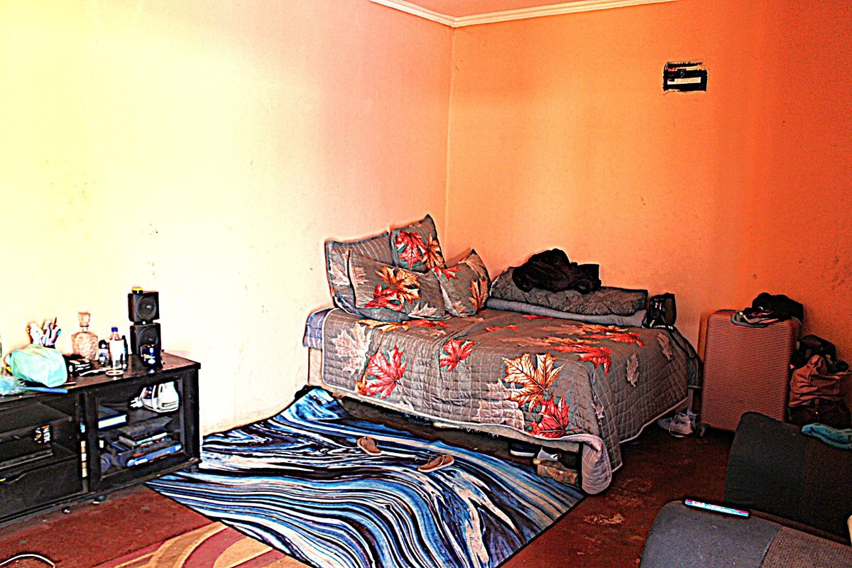A bedroom featuring plain walls and worn flooring, requiring cosmetic updates and repairs to wall finishes.