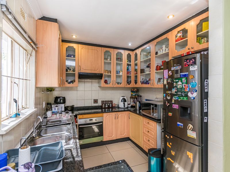 A functional kitchen featuring light wood cabinetry, granite countertops, a built-in oven with hob, and tiled finishes throughout.