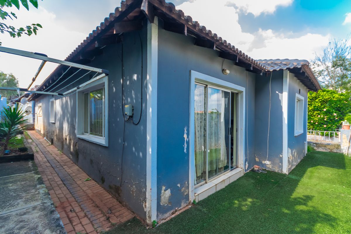 Rear exterior view of the townhouse featuring a sliding door, brick paved walkway, and artificial lawn area requiring maintenance to the exterior wall finish.