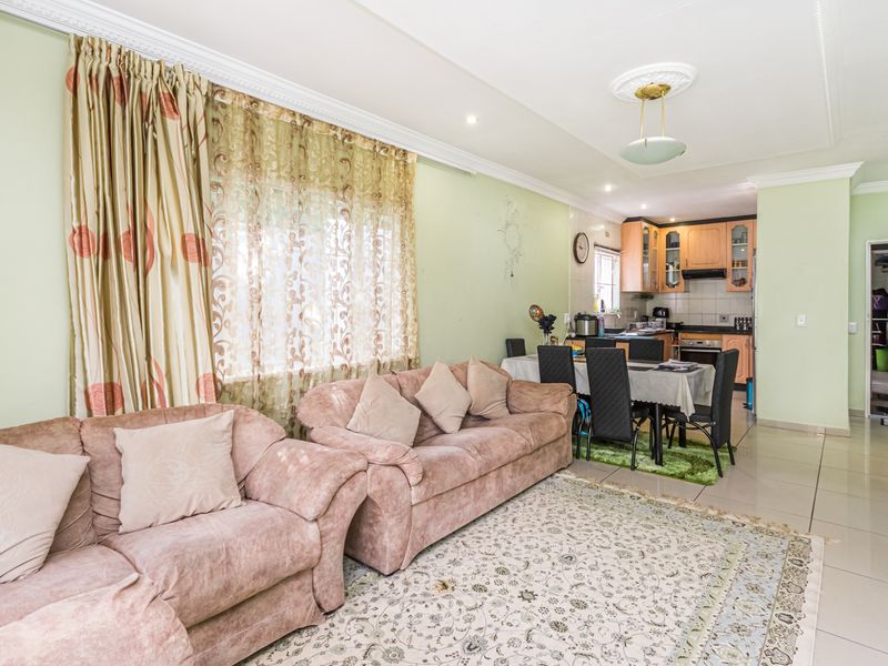 Open-plan living and dining area featuring tiled floors, crown molding, and a functional kitchen with built-in cabinetry and appliances.