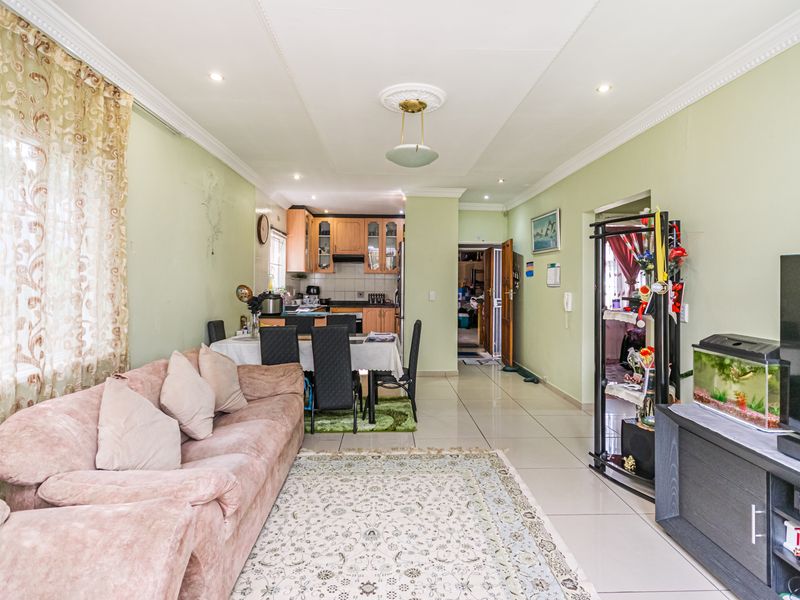 Open-plan living and dining area featuring tiled floors, crown molding, and a connected kitchen with wooden cabinetry.