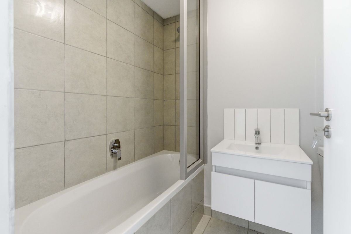A clean, modern bathroom featuring a bathtub with a glass shower screen and a white vanity cabinet with a basin.