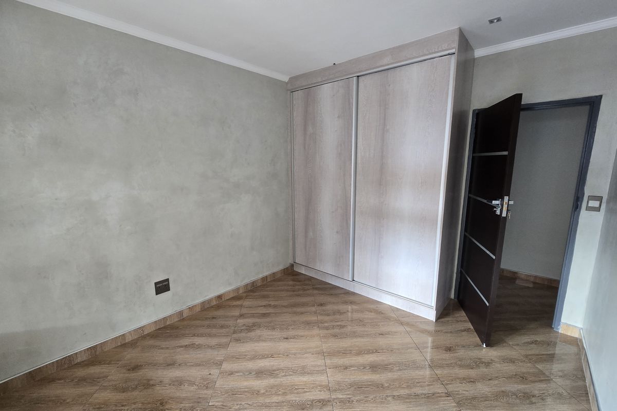 A clean, empty bedroom featuring modern wood-look tiled flooring, a built-in sliding door wardrobe, and neutral grey textured wall finishes.