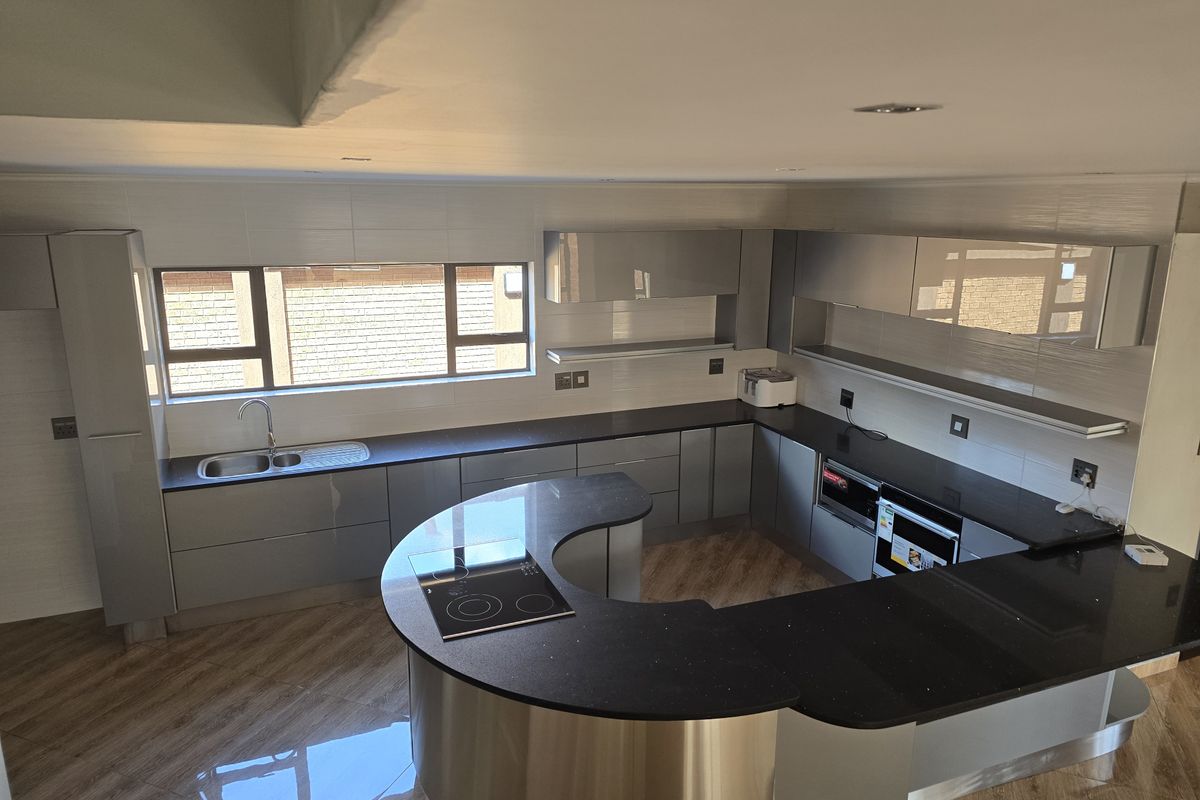 Modern kitchen featuring sleek grey cabinetry, dark stone countertops, a curved breakfast bar with integrated hob, and built-in oven.