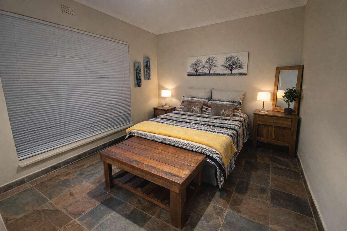 A well-maintained bedroom featuring durable slate tile flooring, neutral wall finishes, and large windows fitted with venetian blinds.