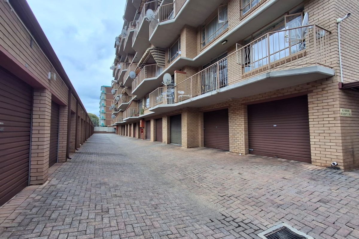 Exterior view of an apartment complex featuring a paved driveway, multiple roller garage doors, and residential balconies with metal railings.