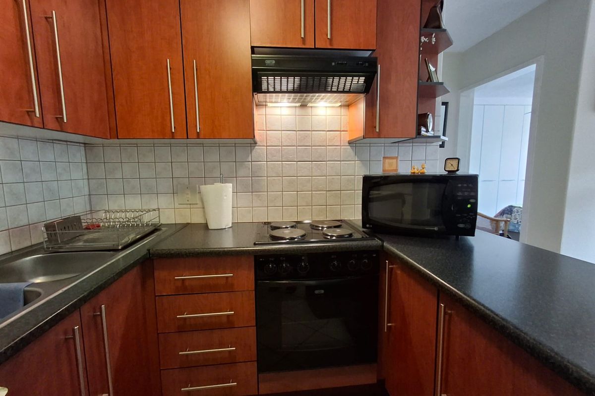 A functional kitchen featuring wood-finish cabinetry, dark laminate countertops, a tiled backsplash, and integrated cooking appliances including an oven and extractor fan.