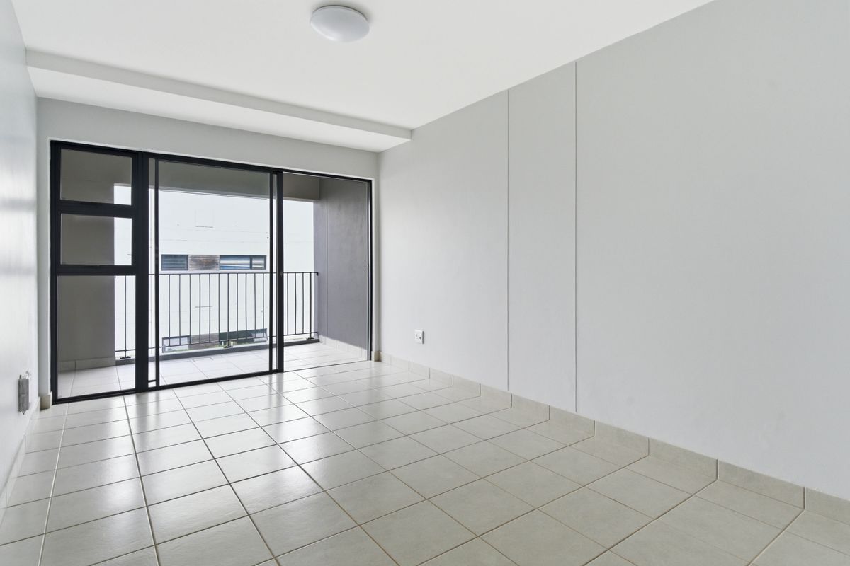 A bright, empty living area featuring neutral tiled flooring and a large sliding glass door providing direct access to a private balcony.