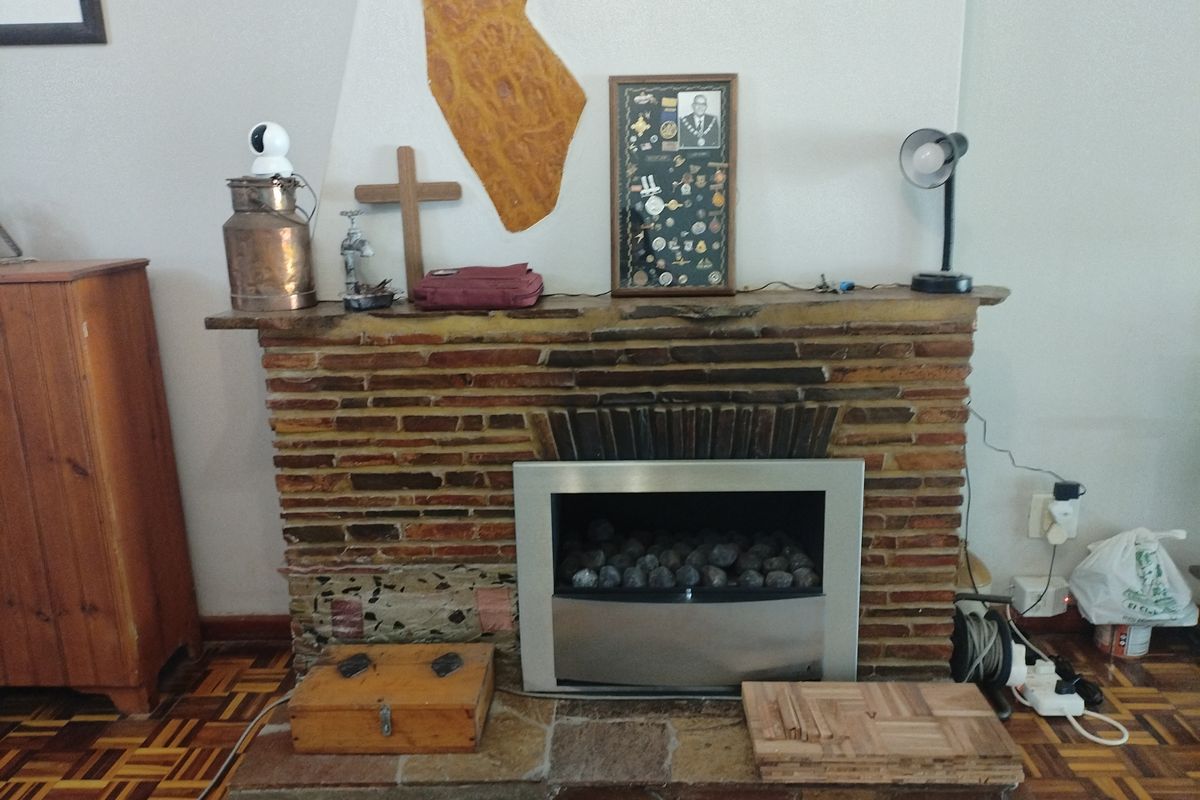 A living room featuring a rustic brick fireplace with a modern stainless steel insert and a traditional parquet wood floor.