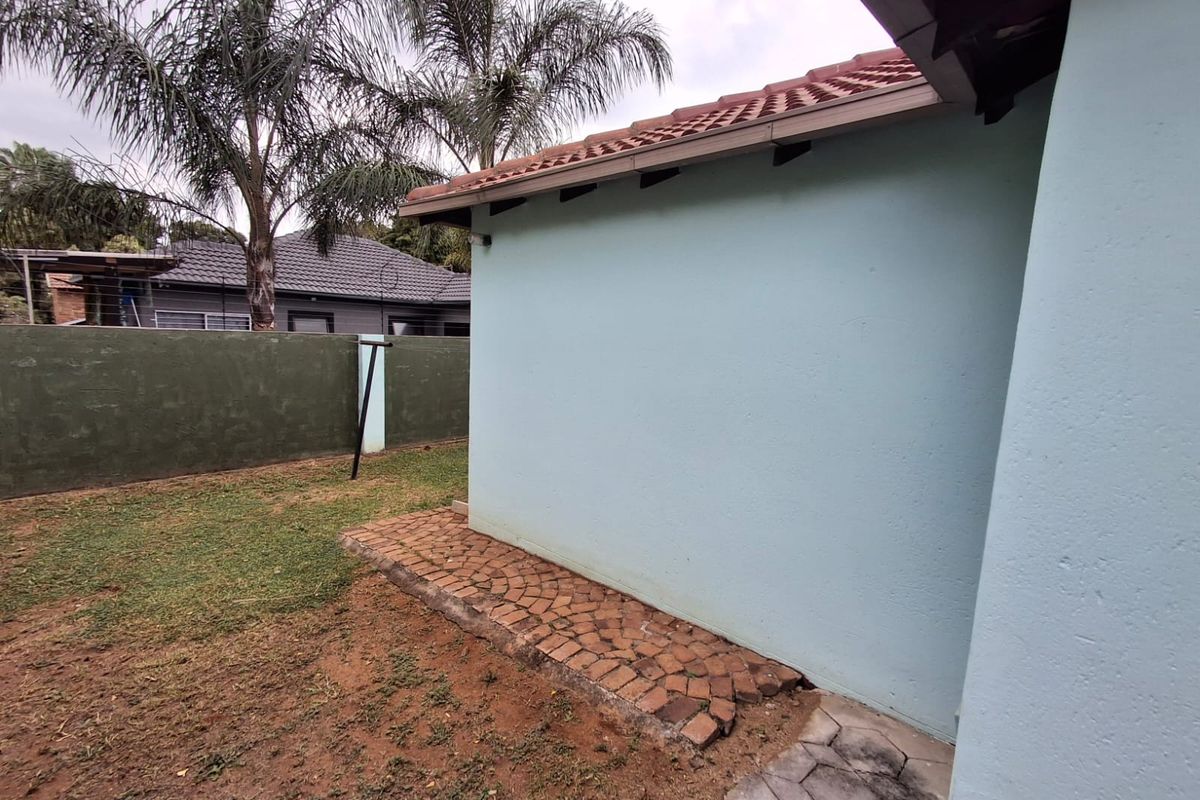 A view of the rear exterior of the house featuring a tiled roof, gutters, and a brick paved walkway alongside a boundary wall.