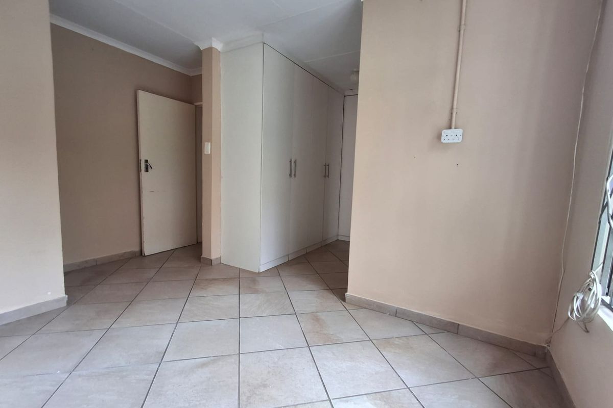 An empty bedroom featuring neutral tiled flooring and built-in white cupboards, providing a clean and versatile space ready for personalization.